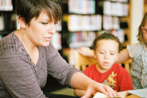 Woman in gray long sleeve shirt sitting beside boy in orange crew neck shirt